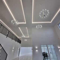 MIAREM - Wnętrze przestronnego, dwukondygnacyjnego holu z marmurową posadzką, białymi ścianami z dekoracyjnymi panelami, czarną balustradą schodów i sufitami z oświetleniem LED oraz kryształowymi żyrandolami.