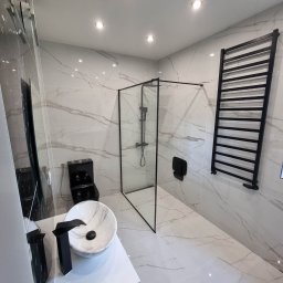 MIAREM - Nowoczesna łazienka wykończona płytkami imitującymi marmur, z czarną armaturą i grzejnikiem drabinkowym, kabina prysznicowa typu walk-in z czarnymi profilami.