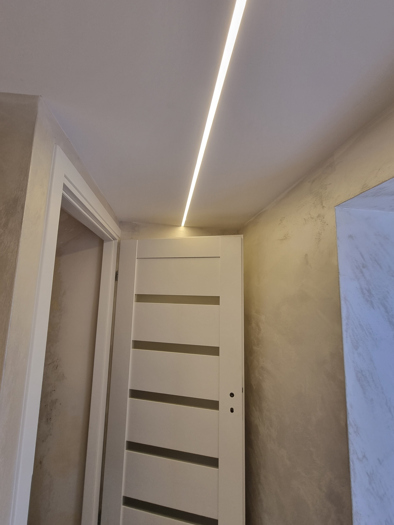 Zamknięte, białe drzwi wewnętrzne z poziomymi przeszkleniami, oświetlenie LED w suficie, ściany wykończone w stylu dekoracyjnym w Rawa Mazowiecka.