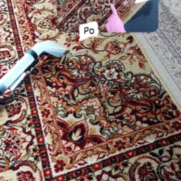 Czyszczenie wzorzystego dywanu metodą ekstrakcyjną, widoczna różnica w kolorze i czystości między obszarem przed i po zabiegu, z użyciem profesjonalnego odkurzacza piorącego z białą ssawką.