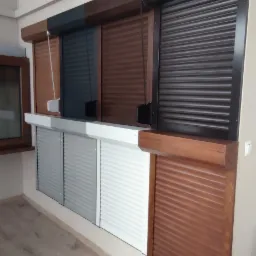 Ekspozycja różnych kolorów i typów osłon okiennych, w tym modeli z drewnianymi ramami i sterowaniem manualnym, prezentowana w showroomie.