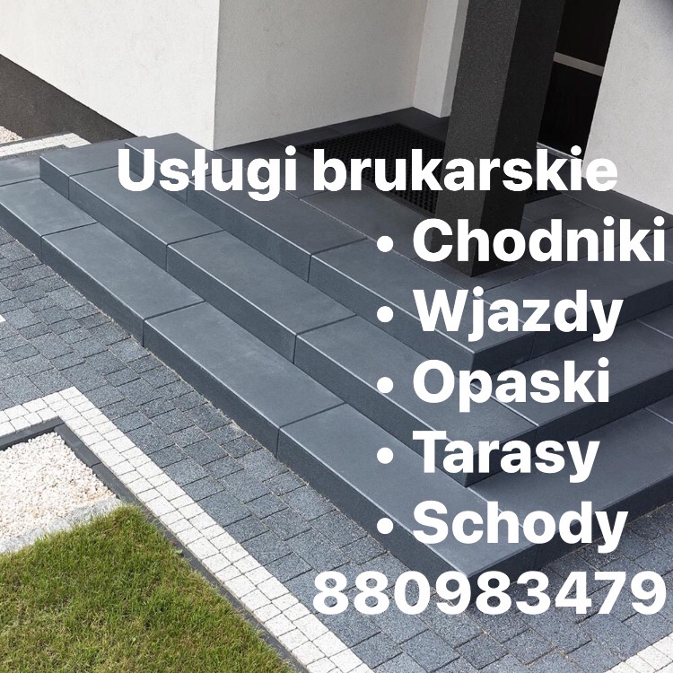 Schody wejściowe wyłożone ciemnoszarą kostką brukową, obok trawnik i jasny pas z drobnego kamienia.