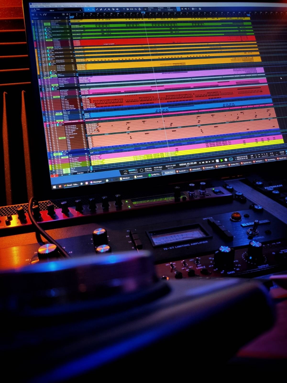 Ekran komputera z otwartym projektem muzycznym w programie DAW, widoczny mikser analogowy z potencjometrami i wskaźnikami w ciemnym pomieszczeniu z nastrojowym oświetleniem.