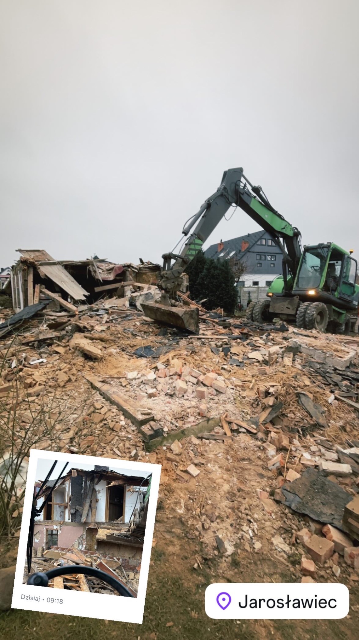Zielona koparka z łyżką na gruzowisku po rozbiórce budynku, w tle fragment zabudowy mieszkalnej i pochmurne niebo. W lewym dolnym rogu wklejone zdjęcie fragmentu rozbieranego budynku.