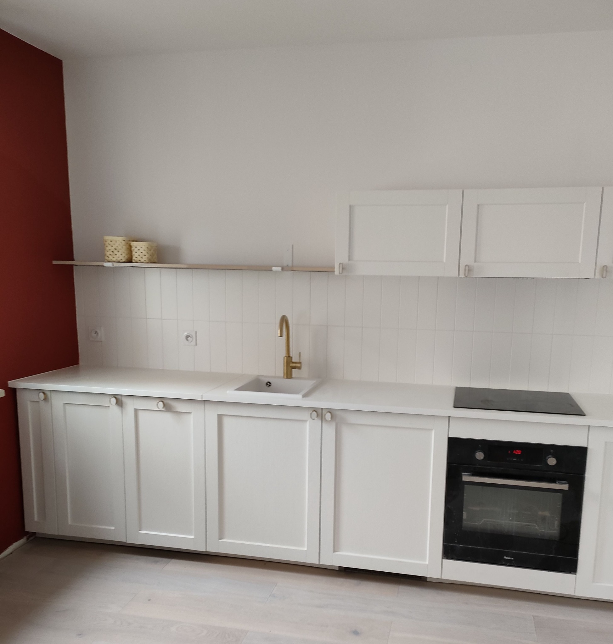 Nowoczesna kuchnia z białymi szafkami, złotą armaturą i ceglastą ścianą w tle, prezentująca minimalistyczny design po remoncie.