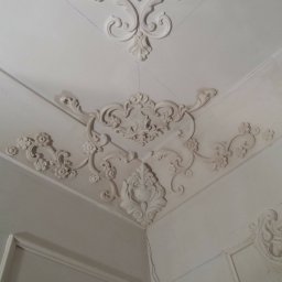 Krzysztof Lis - Dekoracyjne sztukaterie narożne na suficie i ścianach, z delikatnymi śladami ołówka wyznaczającego linie, w białym kolorze.