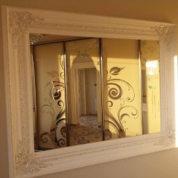 Krzysztof Lis - Wbudowana szafa z przesuwnymi drzwiami, zdobiona ornamentami roślinnymi, widoczna w ozdobnej ramie lustra.