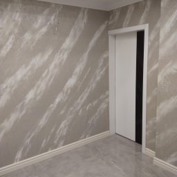 Krzysztof Lis - Wykończone wnętrze z dekoracyjną ścianą w odcieniach szarości z efektem marmuru, białe listwy przypodłogowe i sufitowe oraz szara podłoga imitująca marmur, białe drzwi wewnętrzne.