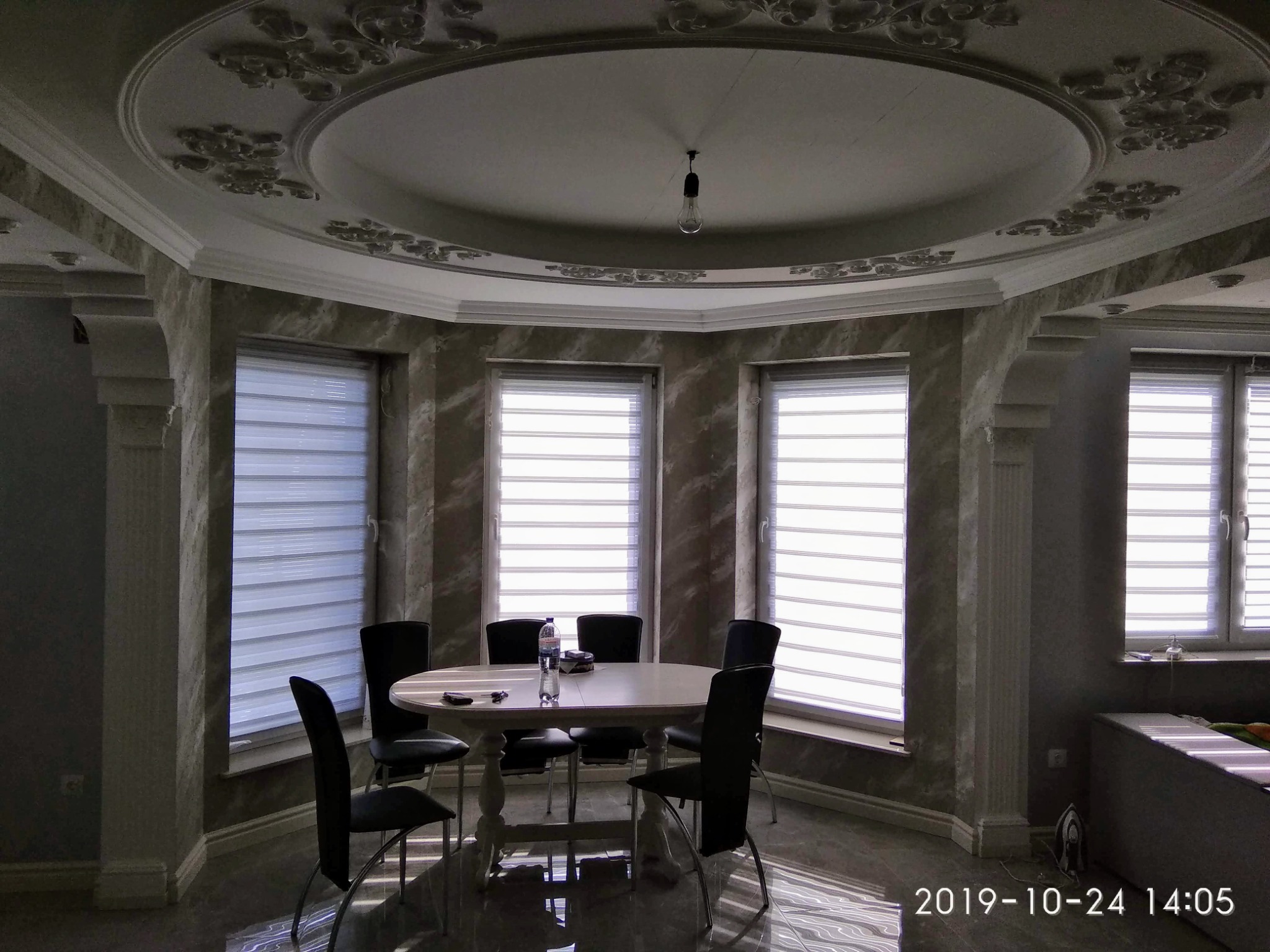 Eleganckie wnętrze jadalni z dekoracyjnym sufitem, marmurkowymi ścianami i żaluzjami okiennymi, oświetlone pojedynczą żarówką