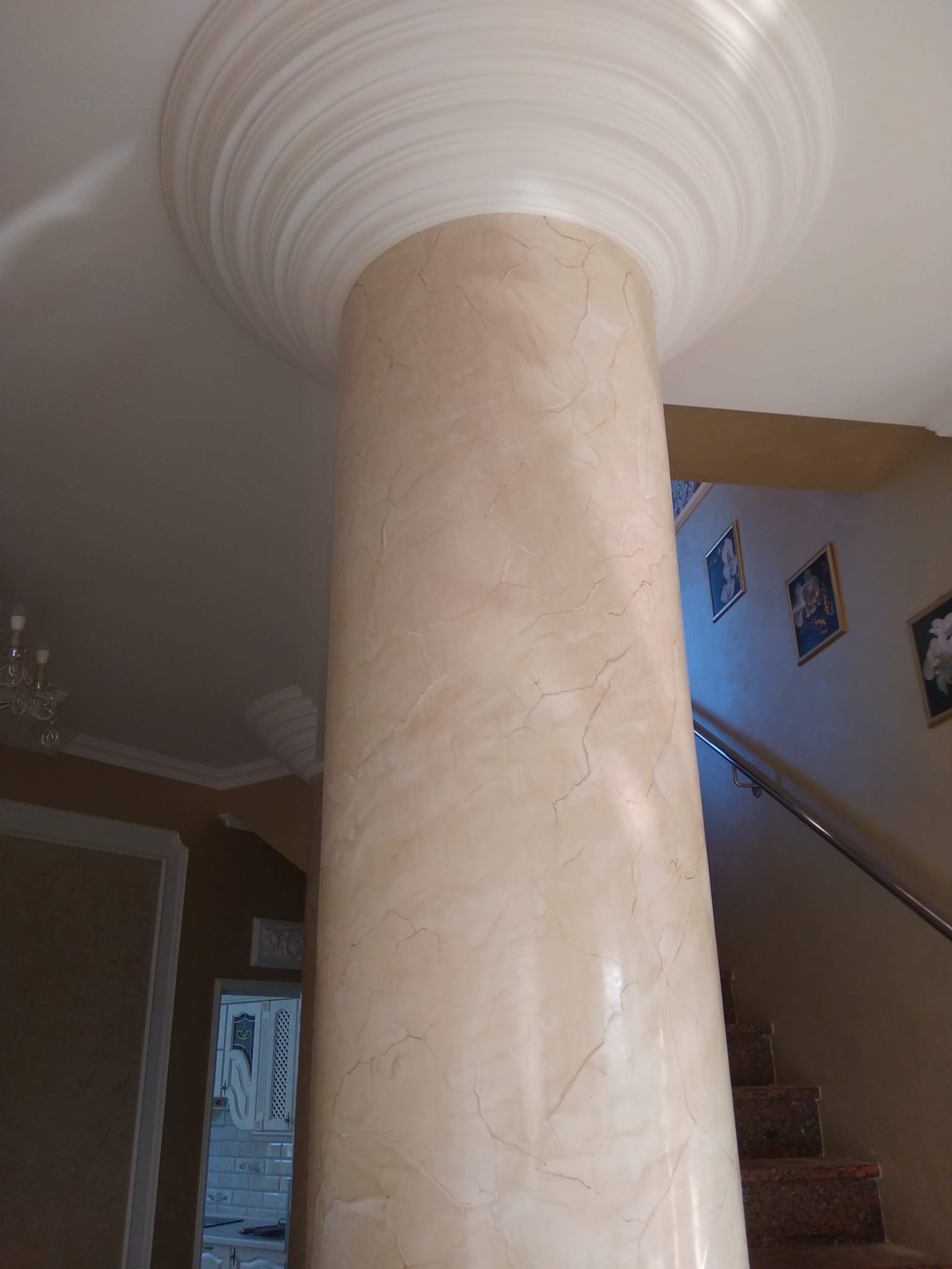 Ozdobna kolumna wewnątrz pomieszczenia z efektem marmuru, zwieńczona dekoracyjnym elementem sufitowym