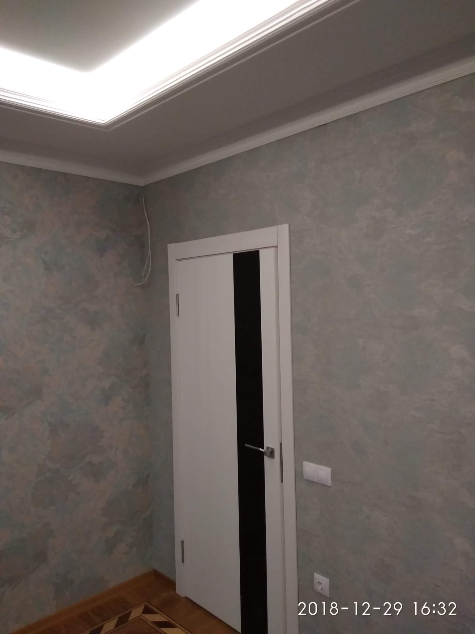 Wnętrze pokoju po odświeżeniu: ściany pokryte dekoracyjną farbą w odcieniach szarości i błękitu, białe drzwi z czarnym pionowym pasem, widoczny fragment podłogi z parkietem w geometryczny wzór...