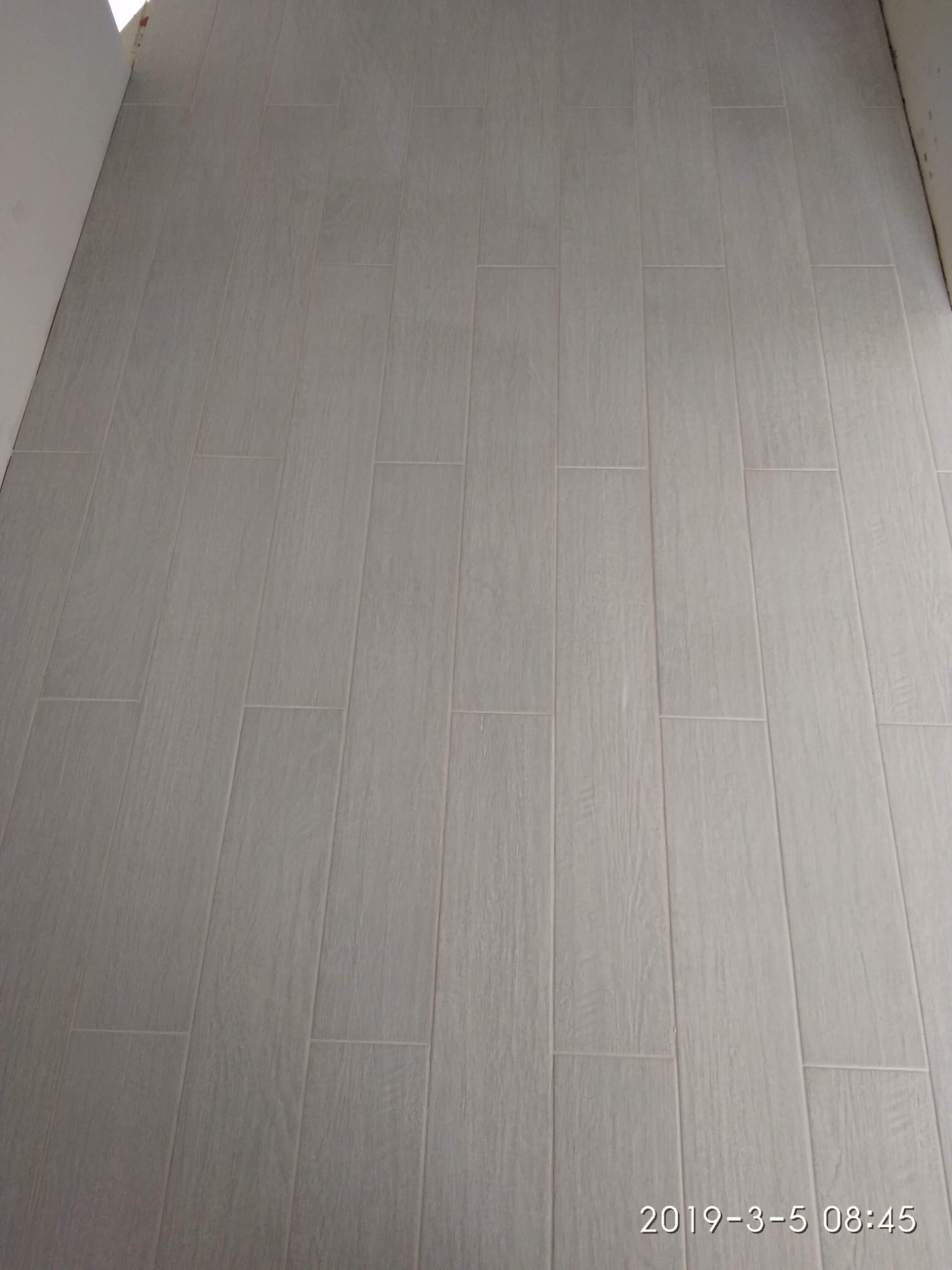 Ułożona podłoga z szarych, podłużnych płytek imitujących drewno, z widocznymi fugami, ułożona wzdłuż pomieszczenia.