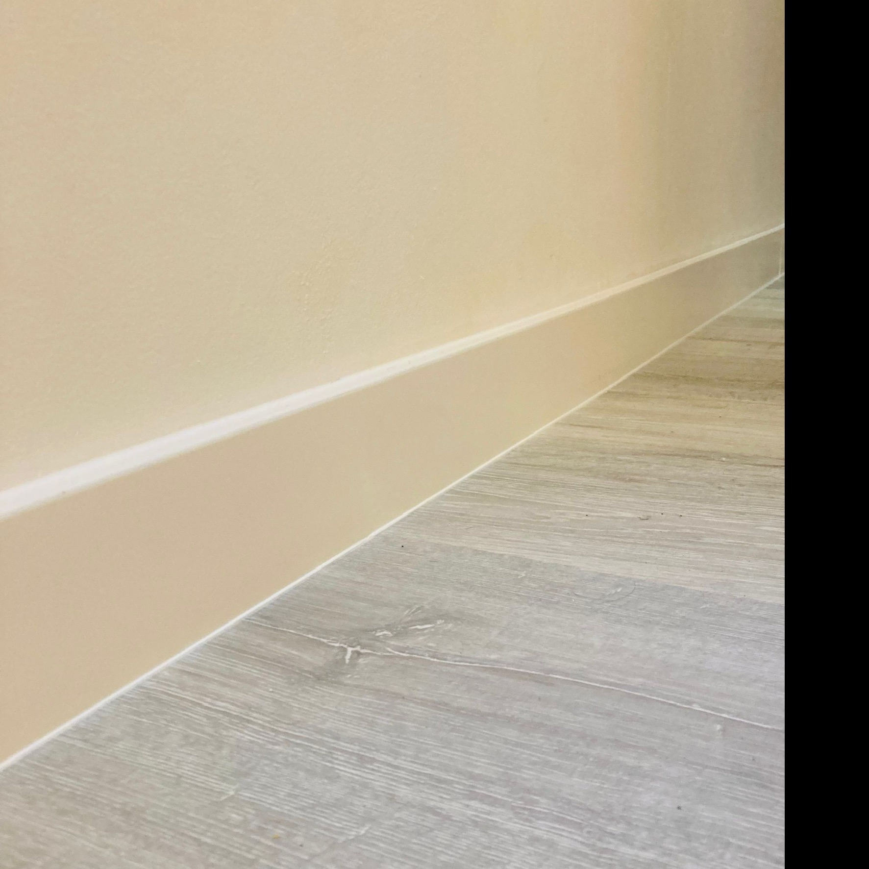 Beżowa ściana z listwą przypodłogową i szara podłoga z paneli imitujących drewno, ujęcie z niskiego kąta.