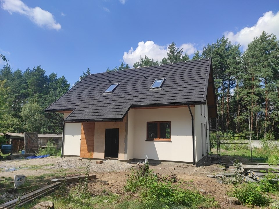 Nowoczesny dom szkieletowy z ciemnym dachem z dwoma oknami dachowymi, zlokalizowany w Olkuszu, otoczony zielenią i drzewami.