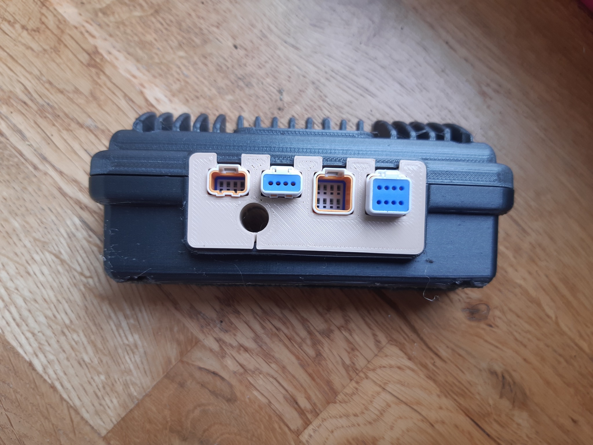 Czarna obudowa z przymocowanymi złączami elektrycznymi, wykonana techniką druku 3D, widoczna na drewnianej powierzchni.