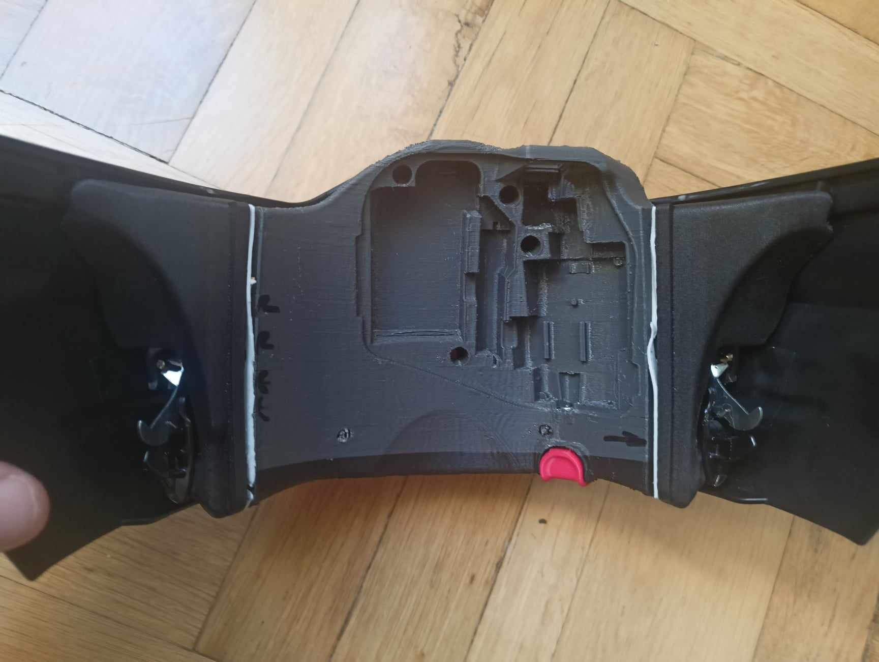 Część samochodowa wydrukowana w technologii 3D, widoczna wewnętrzna struktura i mechanizm mocujący, leżąca na drewnianej podłodze.