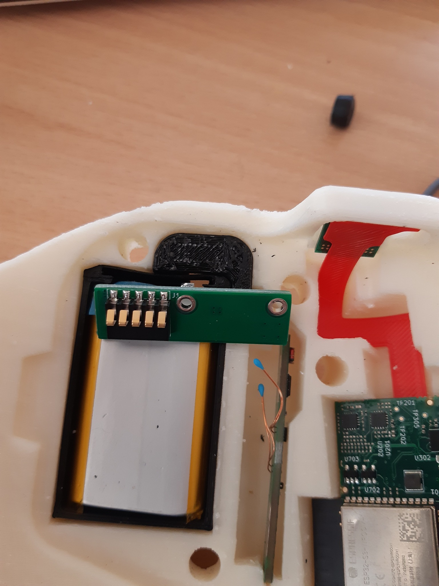 Wnętrze obudowy urządzenia elektronicznego z widocznymi elementami: bateria, płytka drukowana z układami scalonymi, złącza i przewody. Widoczne detale montażowe w obudowie wykonanej prawdopodobnie...