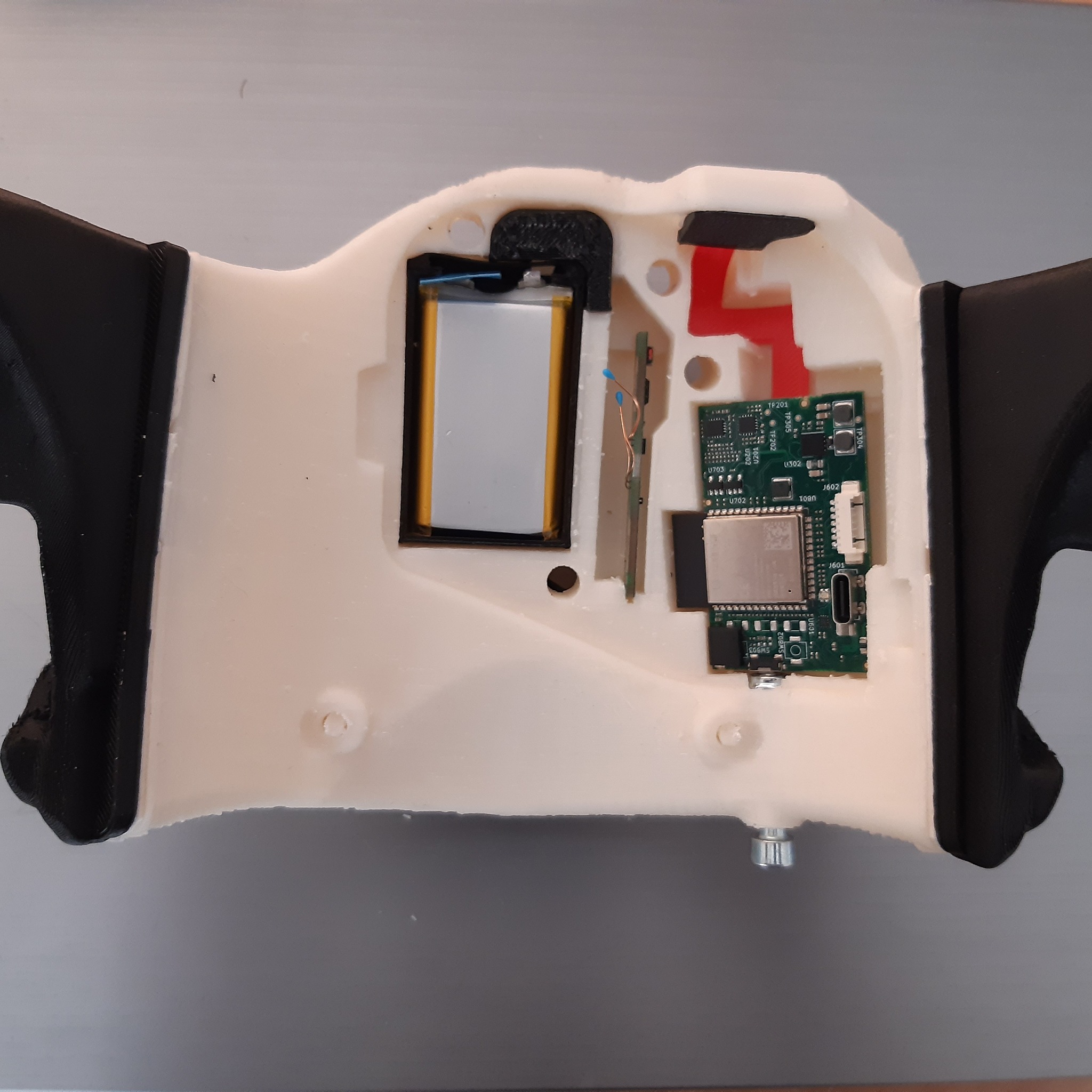 Wnętrze obudowy urządzenia, widoczna bateria, płytka drukowana z elementami elektronicznymi oraz fragmenty obudowy wykonanej z tworzywa sztucznego, prawdopodobnie drukowanej 3D.