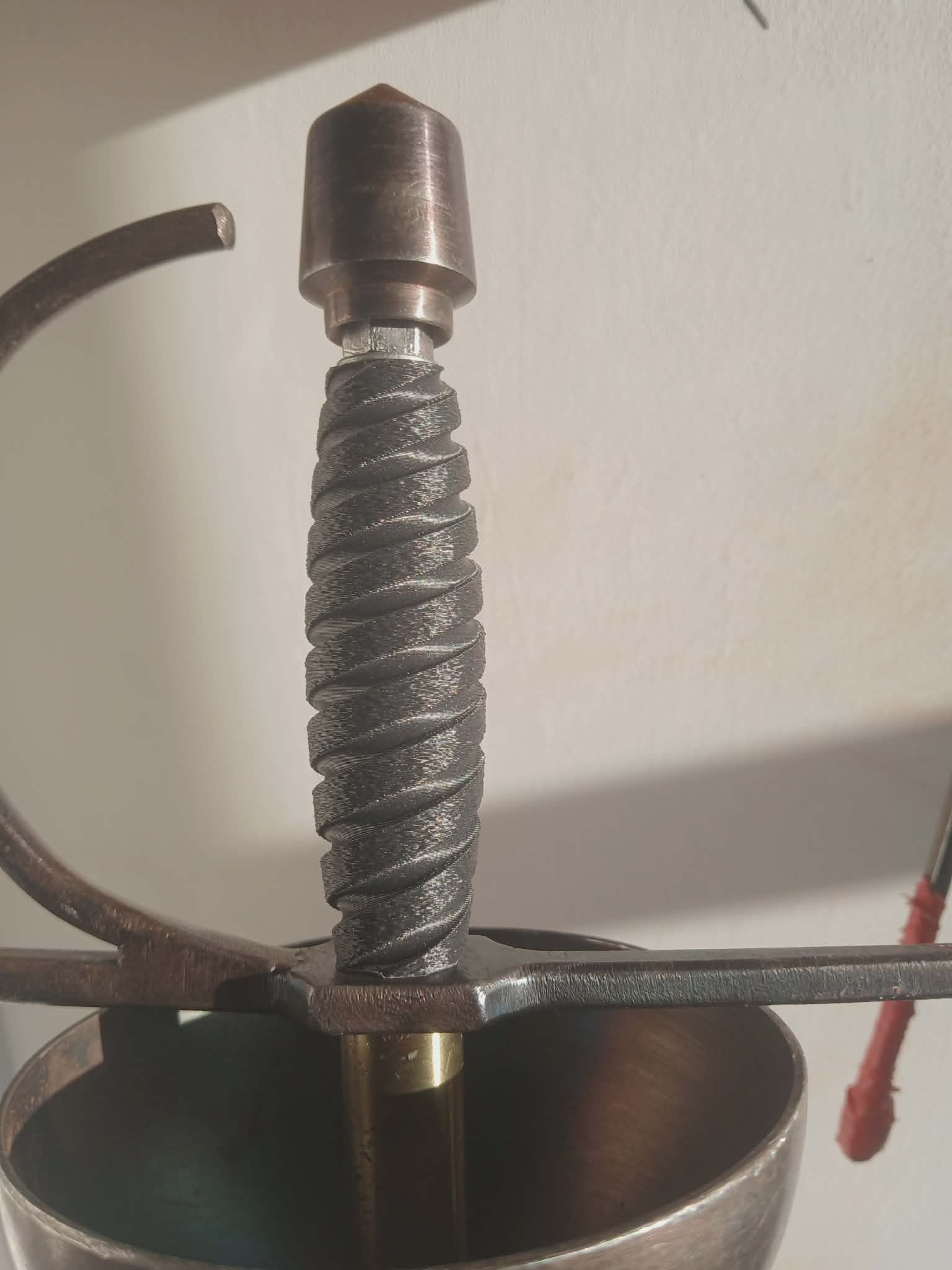 Szczegółowy widok rękojeści szpady z wyraźną fakturą druku 3D, ukazujący spiralne żłobienia i metalowe elementy konstrukcyjne.