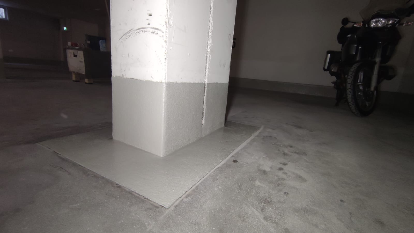 Szary jastrych w garażu podziemnym w Szczecinie, z pomalowanym na szaro słupem i motocyklem w tle.