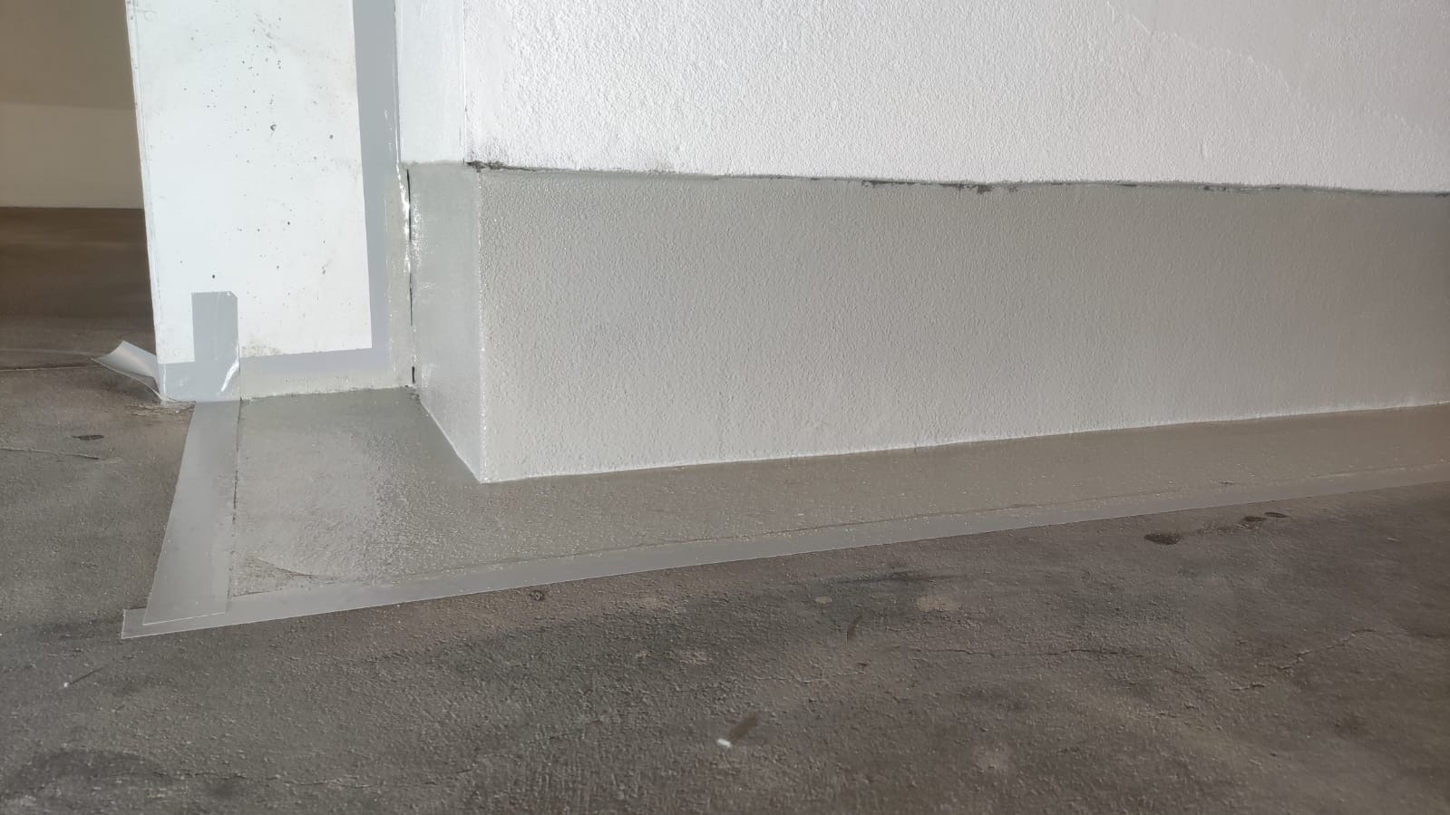 Świeżo wylana, mokra powierzchnia podłogi z widocznymi listwami przypodłogowymi i taśmą ochronną przy ścianach, przygotowana do dalszych prac wykończeniowych.