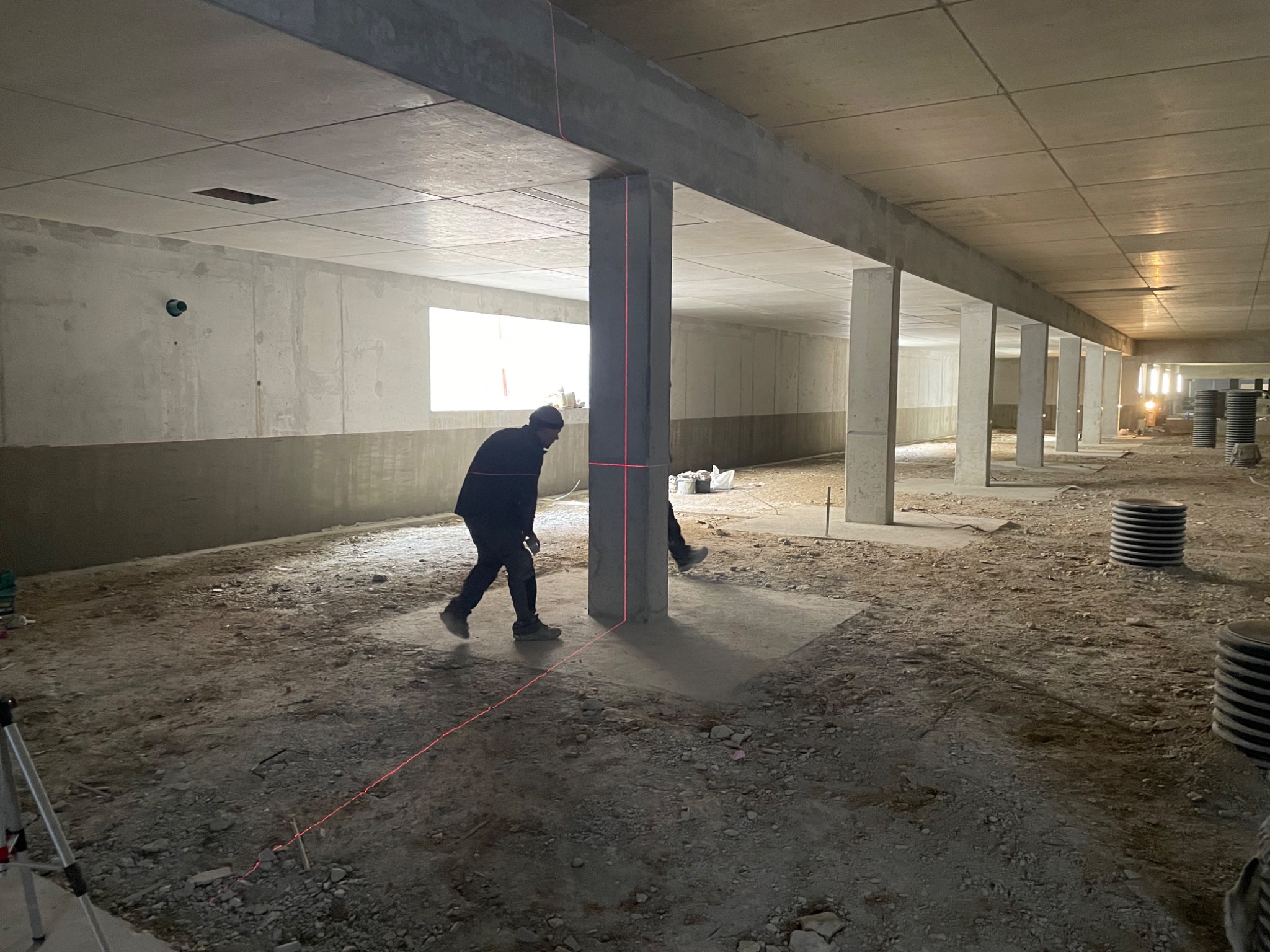 Prace przygotowawcze do wylewki w hali: robotnik z laserowym niwelatorem wyznacza poziom na słupach konstrukcyjnych.