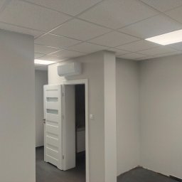 Vitalik Kovalchuk - Wnętrze biurowe po odświeżeniu: pomalowane ściany w odcieniach szarości, białe drzwi z przeszkleniami, sufit podwieszany z oświetleniem LED i klimatyzator.