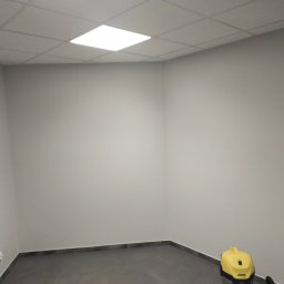 Vitalik Kovalchuk - Pomieszczenie po malowaniu ścian na szaro, widoczny szary panel podłogowy i odkurzacz przemysłowy Karcher w rogu.