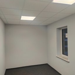 Vitalik Kovalchuk - Pomalowane na szaro wnętrze pokoju z szarą wykładziną dywanową, białym oknem z marmurowym parapetem i kasetonowym sufitem z wbudowanym oświetleniem.