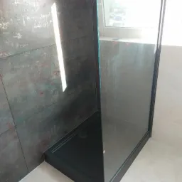 Kabina prysznicowa z czarnym brodzikiem i szklanymi ściankami, rustykalne ciemne płytki na ścianie, jasne płytki podłogowe, widok z niskiego kąta.