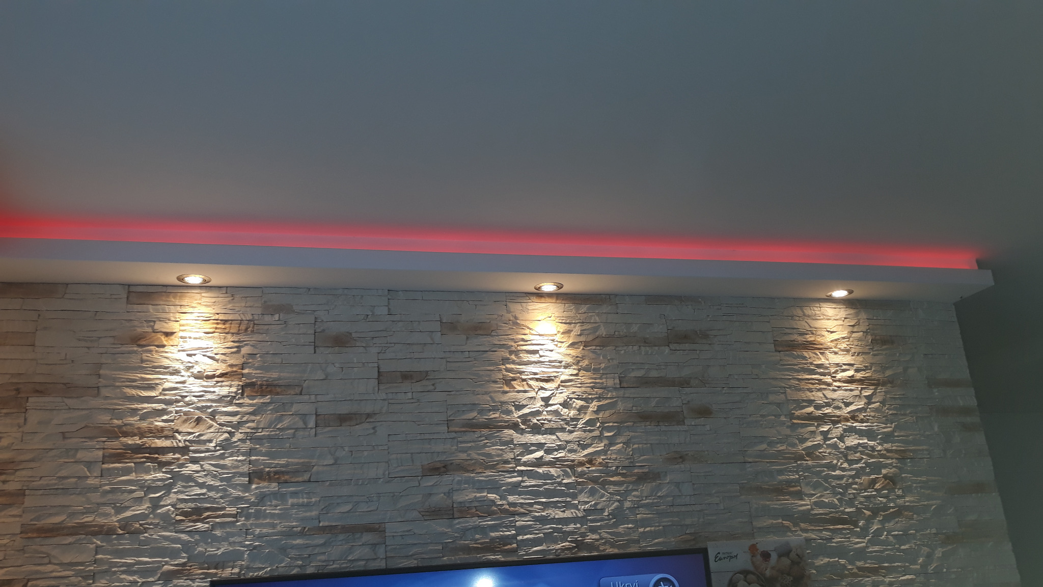 Ściana wykończona dekoracyjnym kamieniem z podświetleniem LED i trzema punktowymi lampami halogenowymi w suficie.