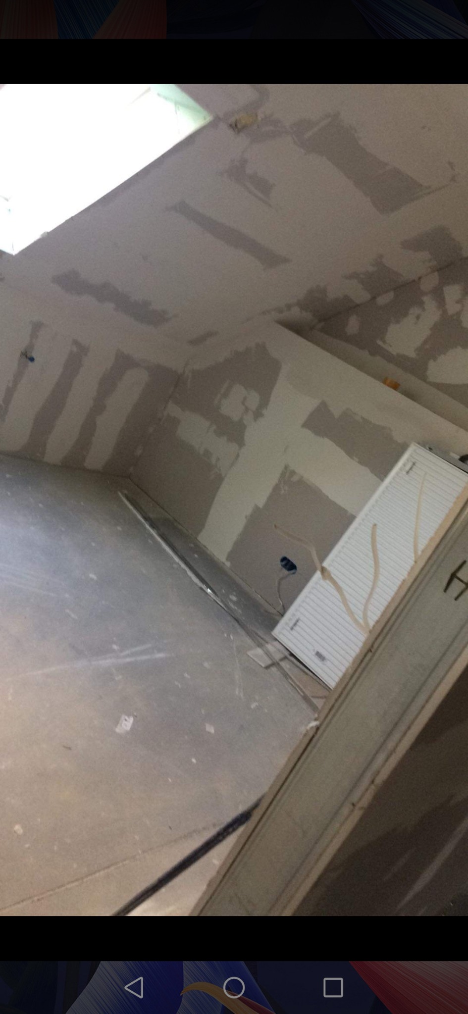 Surowy stan wnętrza z płytami kartonowo-gipsowymi na ścianach i suficie, widoczne ślady szpachlowania, instalacja elektryczna i grzejnik, przygotowane do dalszych prac wykończeniowych.