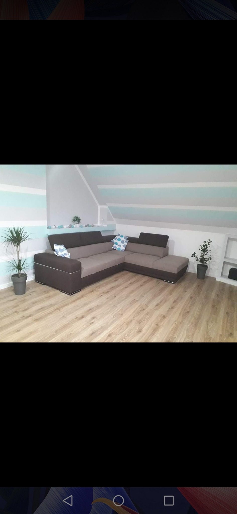 Szaro-brązowy narożnik w pokoju na poddaszu z drewnianą podłogą i pomalowanymi w poziome pasy ścianami. Dwie rośliny doniczkowe po bokach narożnika.