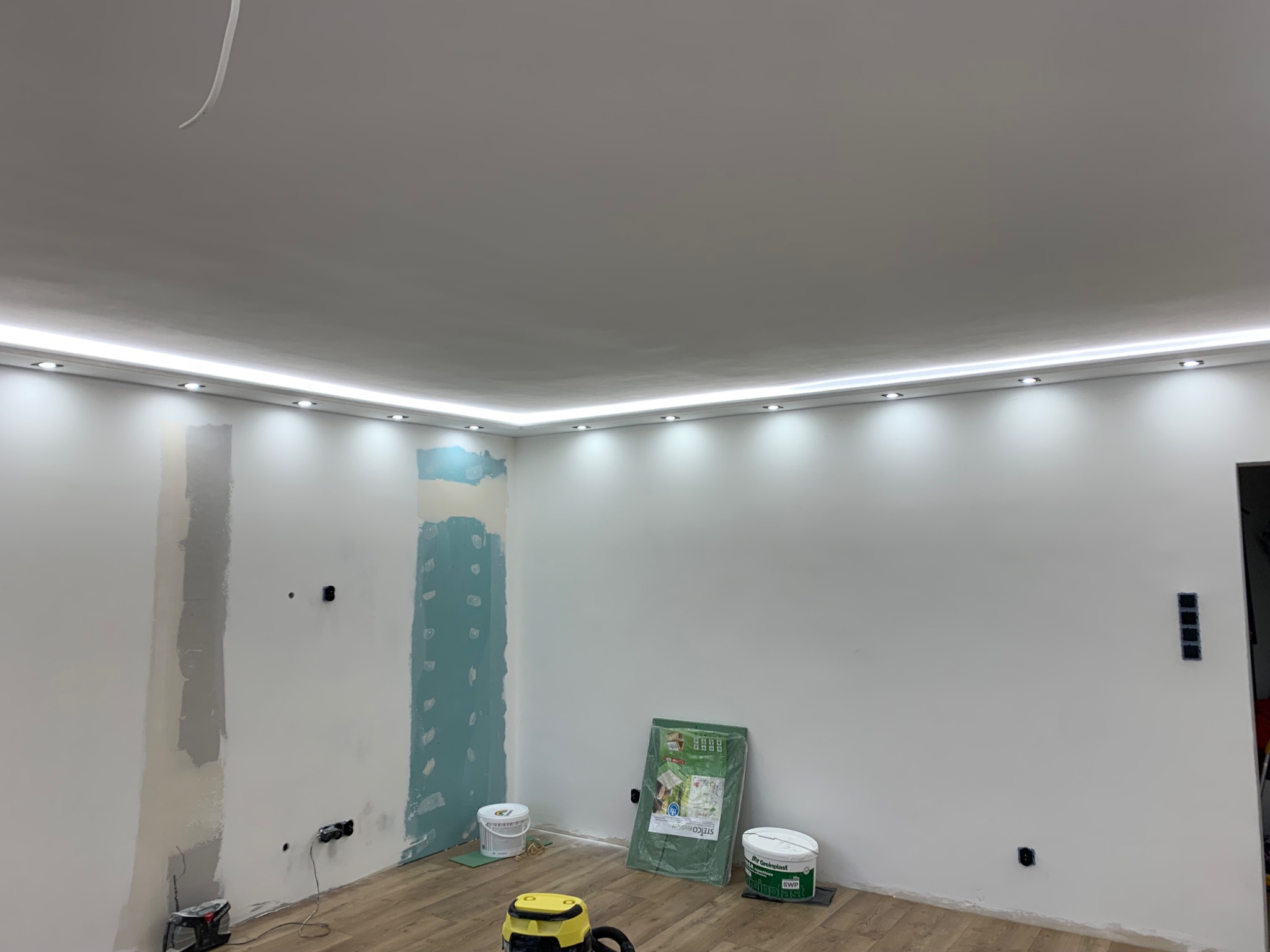 Wnętrze w trakcie remontu w Nowej Wsi Malborskiej: ściany częściowo wyszpachlowane i pomalowane na biało, sufit z oświetleniem LED, widoczne narzędzia i materiały budowlane na podłodze.