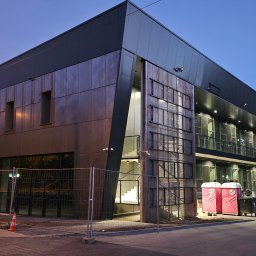 AVISTAL SPÓŁKA Z OGRANICZONĄ ODPOWIEDZIALNOŚCIĄ - Nowoczesny budynek biurowy z płyt warstwowych w szaro-brązowej kolorystyce, oświetlony wieczornym światłem, z widocznymi detalami wykończenia i elementami infrastruktury.