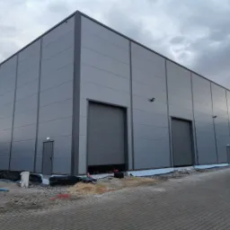 Nowoczesny budynek przemysłowy z szarych płyt warstwowych w Rzeszowie, z widoczną częściowo otwartą bramą segmentową i metalową drabinką na elewacji bocznej.