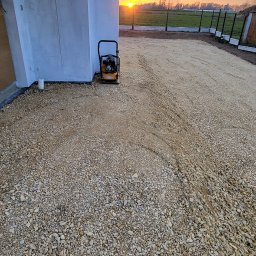 Dawidmirek - Przygotowanie podłoża z kruszywa pod kostkę brukową, widoczna ubijarka wibracyjna i zachodzące słońce.