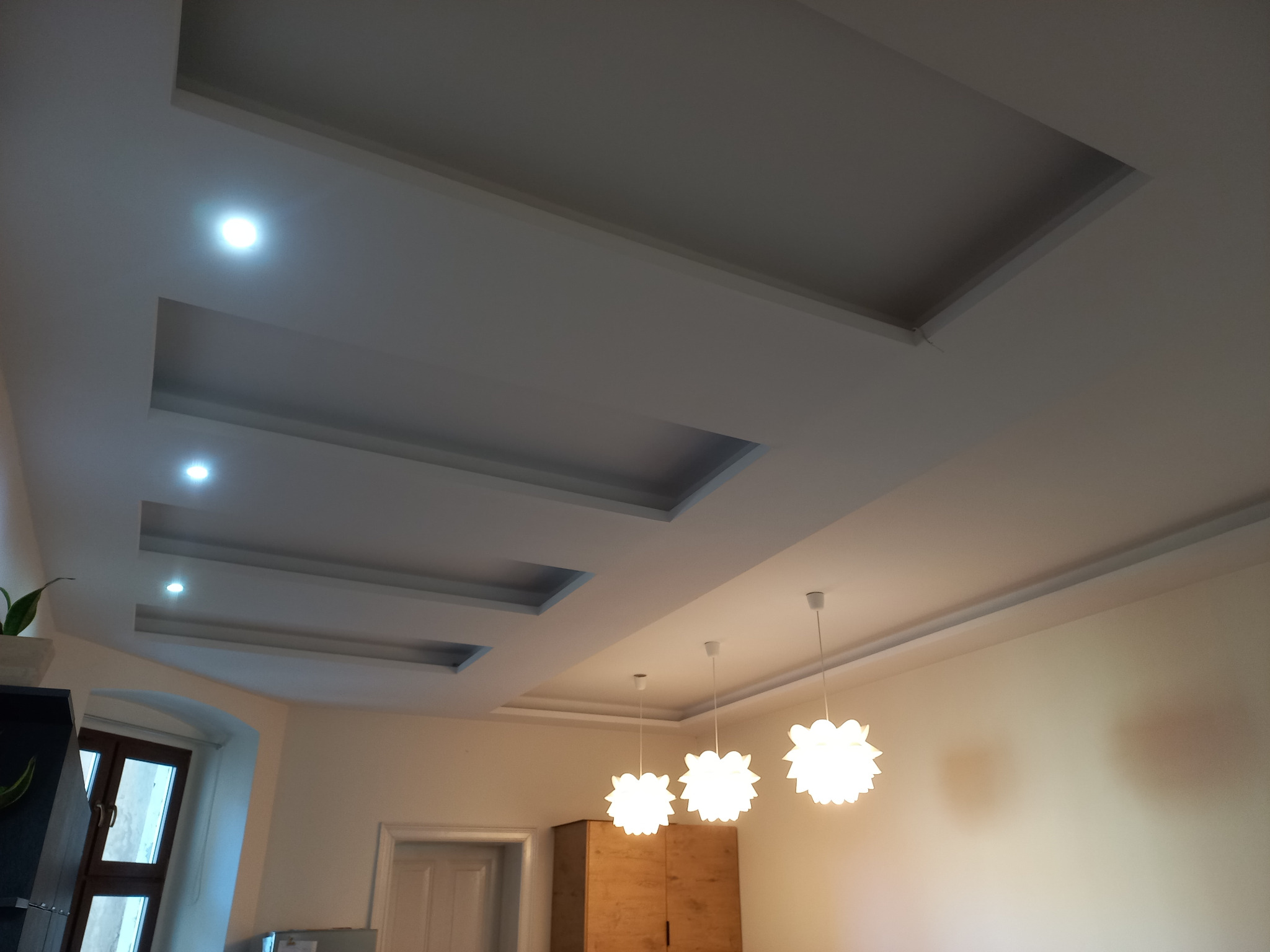 Nowoczesny sufit podwieszany z wbudowanym oświetleniem punktowym i trzema dekoracyjnymi lampami wiszącymi w Legnicy, widok z dołu.