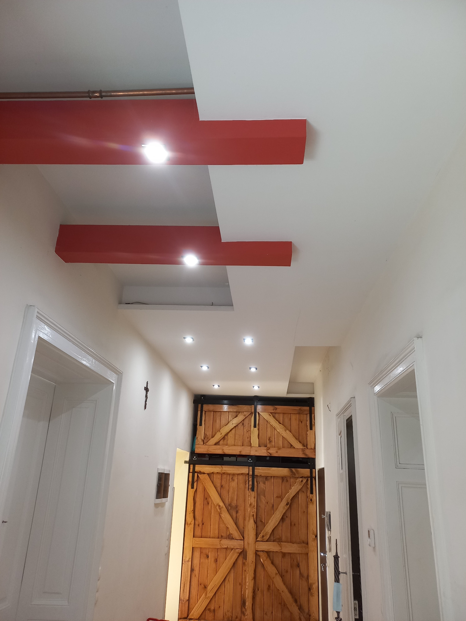 Korytarz z drewnianymi drzwiami przesuwnymi typu stodoła, białe ściany, czerwone belki dekoracyjne na suficie i wpuszczane oświetlenie.