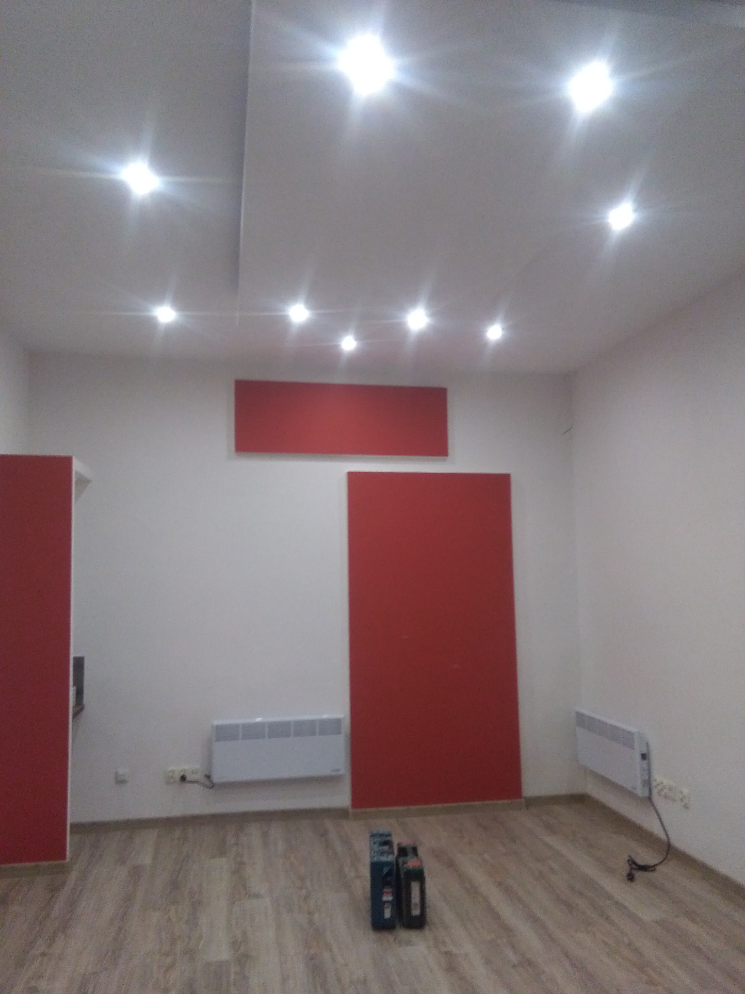 Wnętrze pokoju po remoncie z panelami podłogowymi, czerwonymi elementami dekoracyjnymi na ścianie i oświetleniem sufitowym