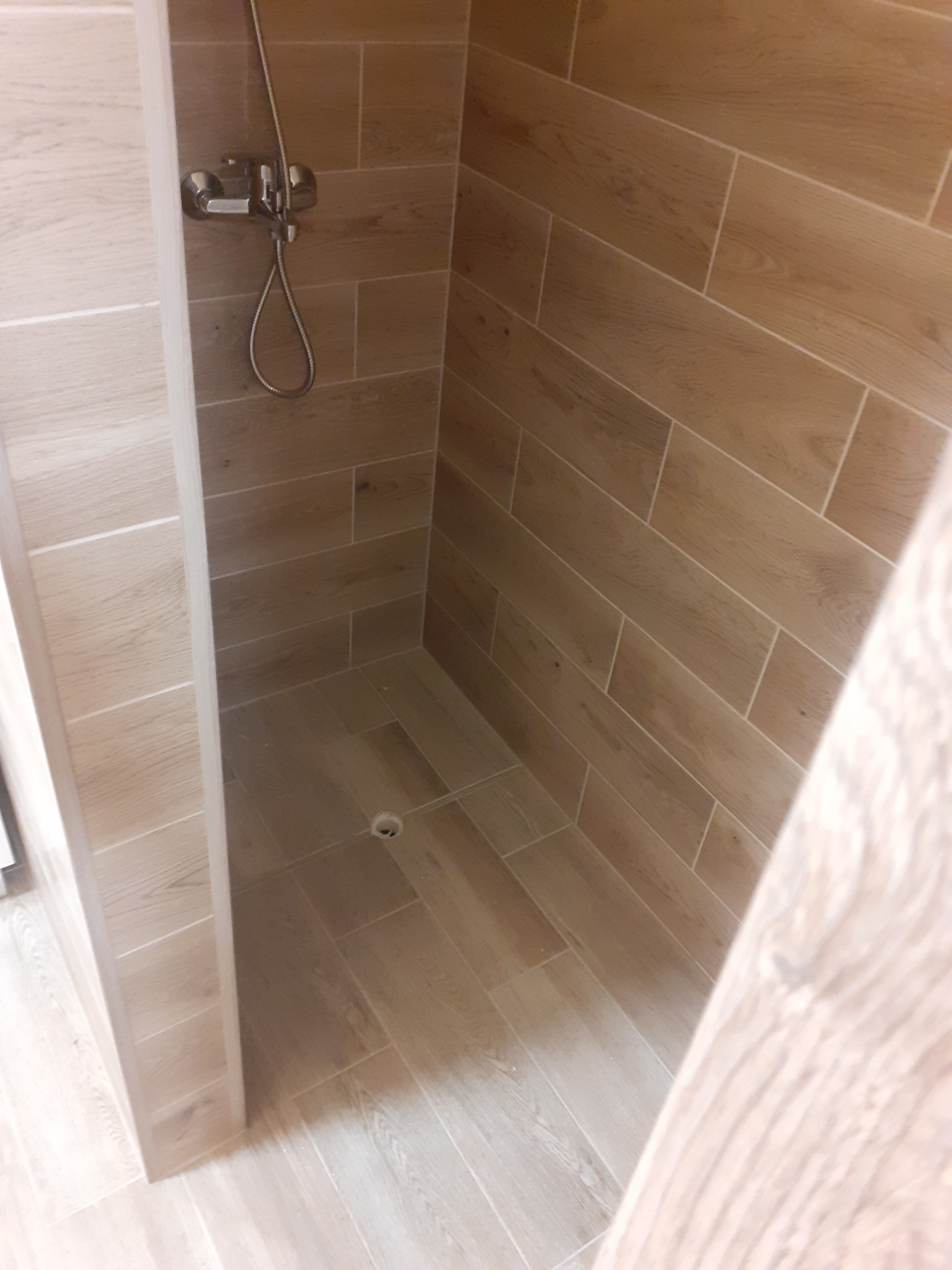 Wnętrze kabiny prysznicowej wyłożonej płytkami imitującymi drewno, z widoczną armaturą i odpływem liniowym.