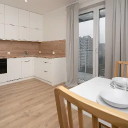 Jasna kuchnia z drewnianym blatem, widok na stół z zastawą i budynki za oknem.