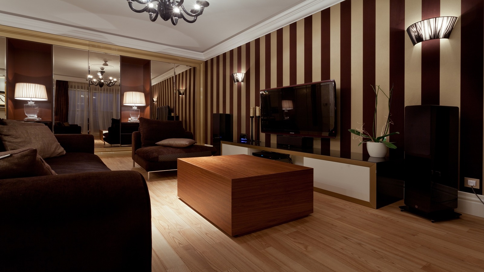 Elegancki salon z brązowymi meblami, drewnianym stolikiem kawowym i ścianą w pionowe pasy, lustrzana szafa w tle powiększa optycznie przestrzeń.