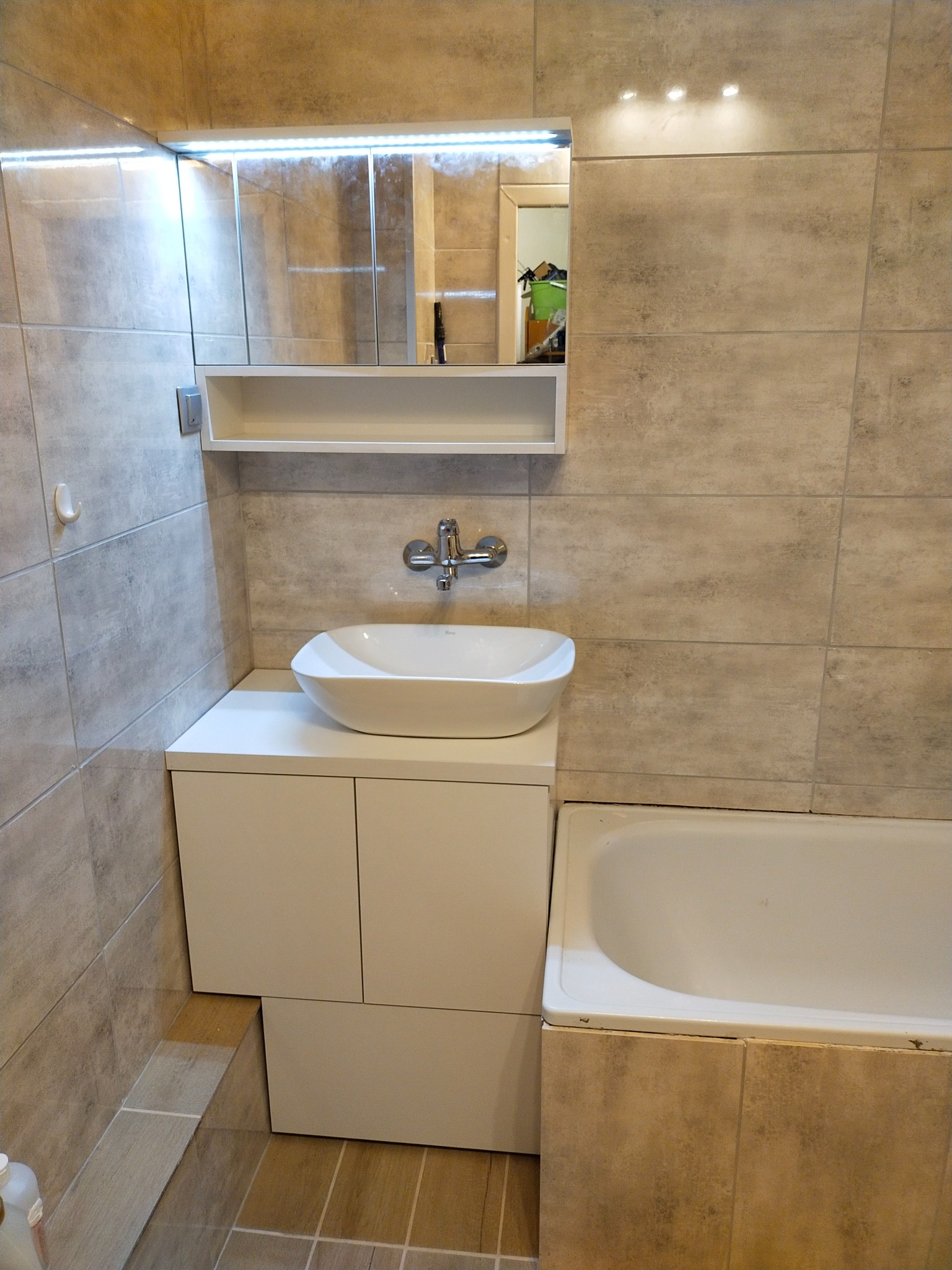 Nowoczesna łazienka z umywalką nablatową na szafce z białymi frontami, lustro z oświetleniem LED i płytki imitujące kamień.