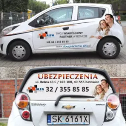 Biały samochód Chevrolet Spark z reklamą firmy ubezpieczeniowej Alfa na boku i tyle, prezentujący logo, dane kontaktowe i uśmiechniętą parę.