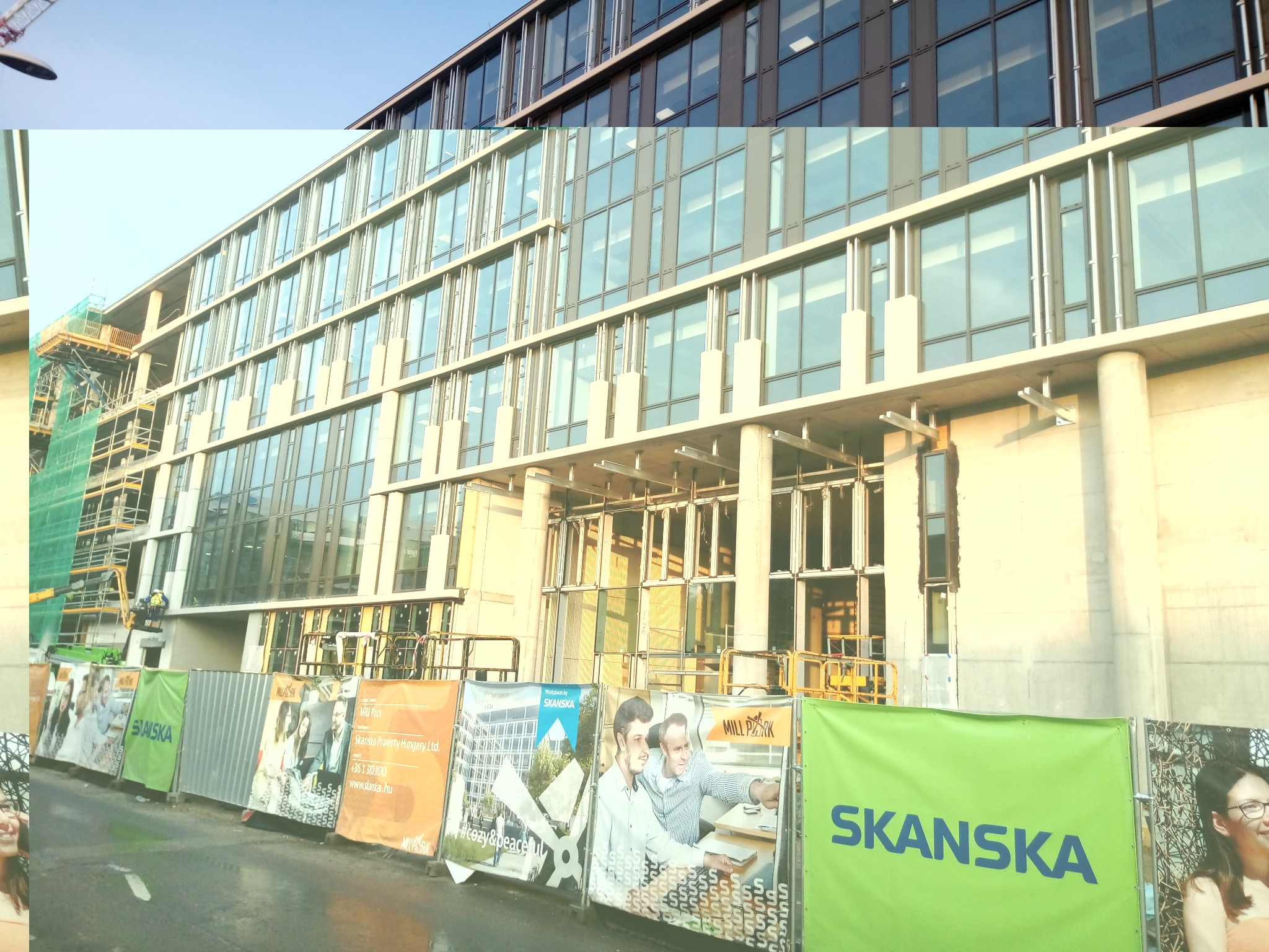 Budynek biurowy w trakcie budowy z widocznymi oknami, rusztowaniami i banerami reklamowymi firmy Skanska.