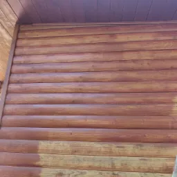 Malowanie drewnianej elewacji domu na brązowo; widoczna różnica w kolorze między pomalowaną a niepomalowaną częścią ściany.