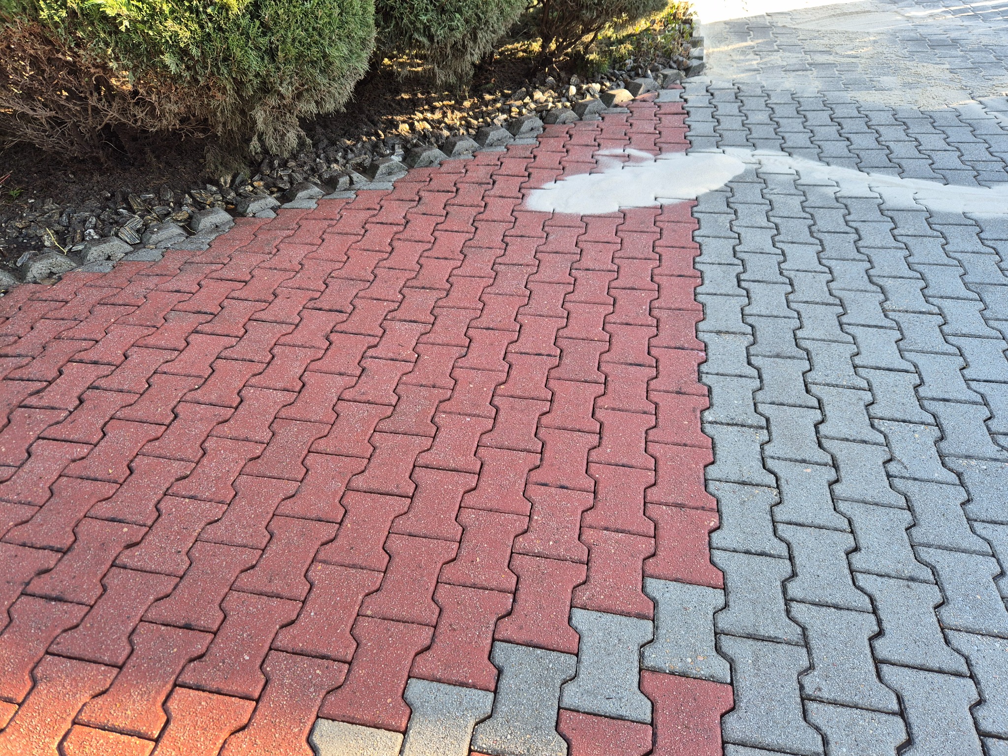 Czerwono-szara kostka brukowa po myciu w Bielsko-Białej, widoczna różnica w czystości. Część kostki czerwona, część szara, obok krzewy.