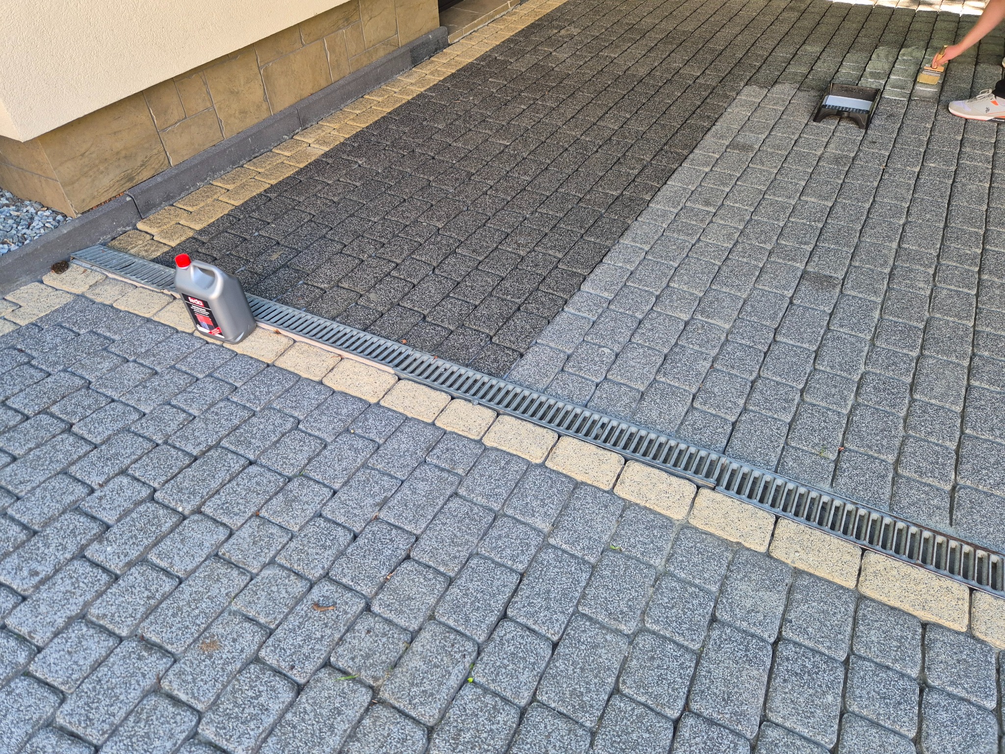 Impregnacja kostki brukowej: fragment posesji z wyczyszczoną i zaimpregnowaną kostką, widoczna butelka impregnatu i pędzel. Część kostki jest jeszcze niezaimpregnowana.