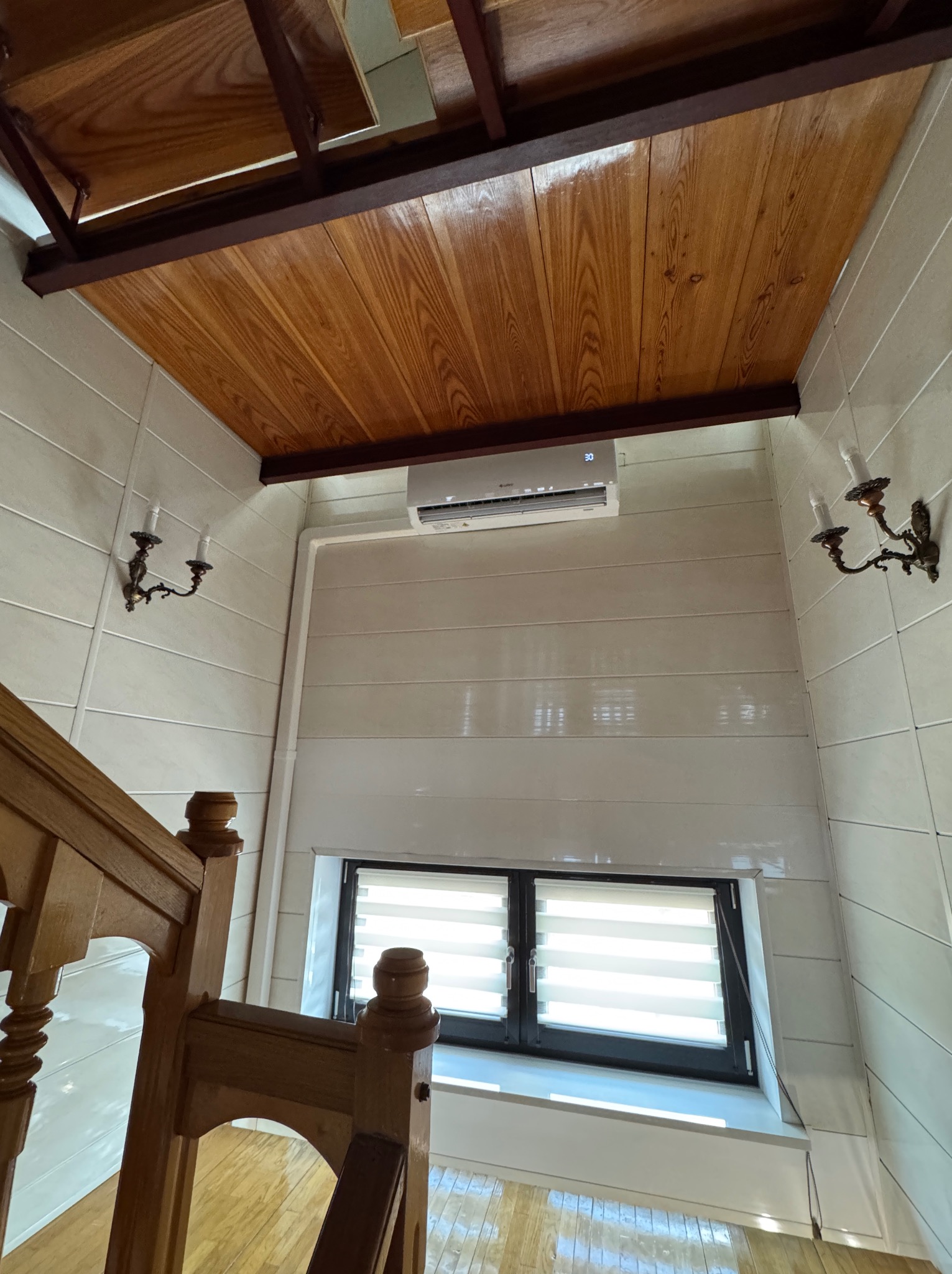 Wnętrze klatki schodowej z zainstalowanym klimatyzatorem ściennym, drewnianym sufitem i kinkietami w stylu retro.